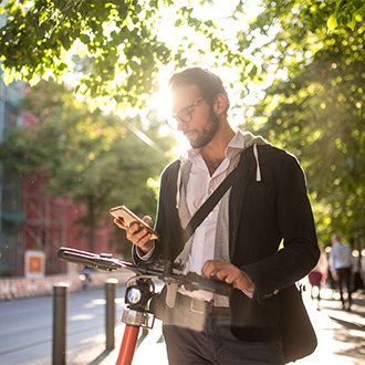 homme tenant une trottinette et consultant son téléphone portable