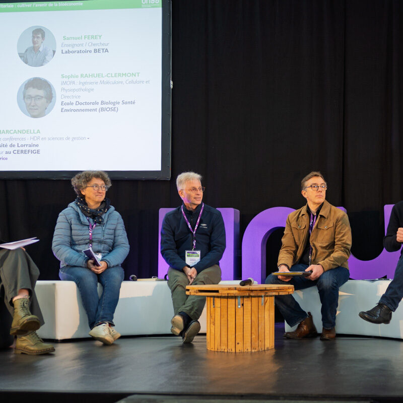 Un intervenant prend la parole. Ils sont assis sur scène